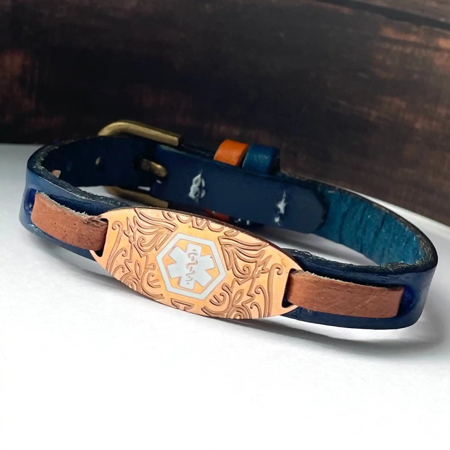 A blue leather medical alert bracelet with a decorative copper-colored identification plate.